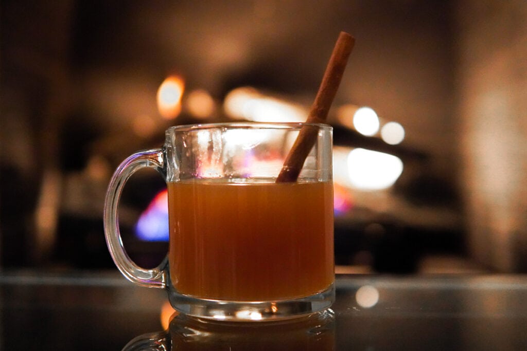 Warm Spiked Apple Cider in Clear Mug in front of fire