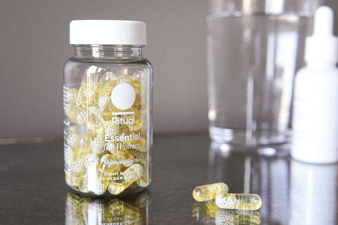 Ritual Multivitamins in bottle on mirror table with drinking glass behind