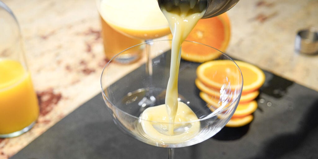 Pouring orange creamsicle martini into coupe glass