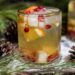 White holiday sangria with orange, pear and pomegranate surrounded by pine, snow and pinecones.