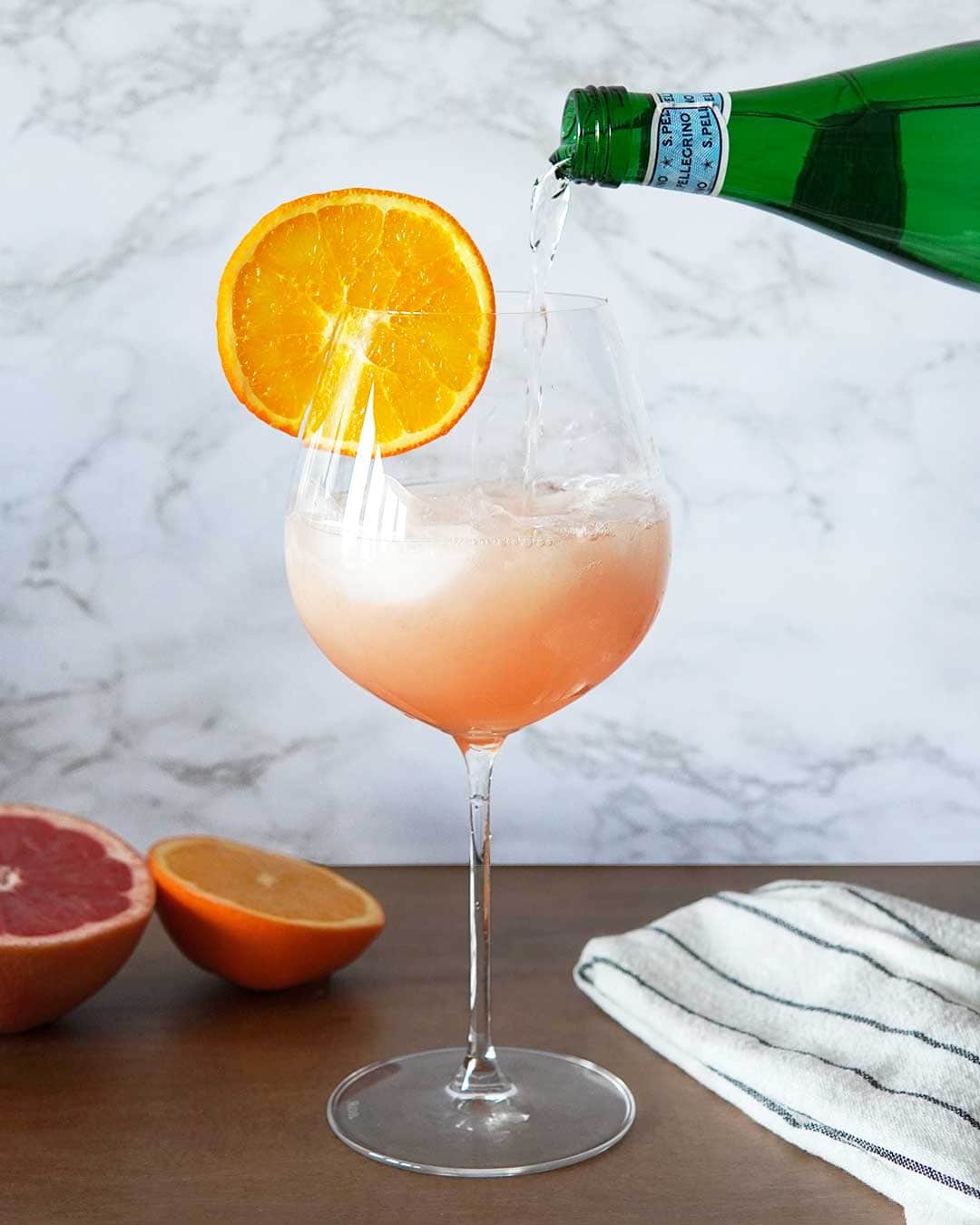 Aperol Sprtiz Mocktail in wine glass on wood table and marble background.
