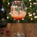 Spiced Cranberry Pear Spritz in wine glass with sugared cranberries and rosemary sprig in front of christmas tree