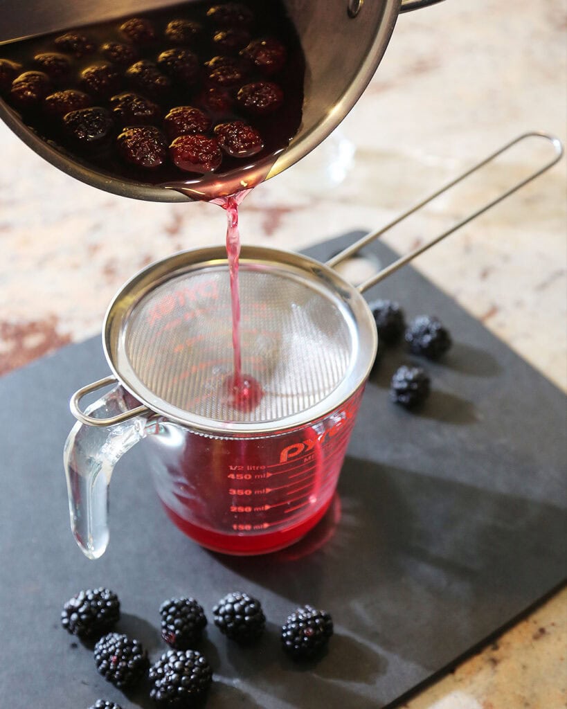 Blackberry simple syrup strained through a fine mesh sieve into a glass measuring cup