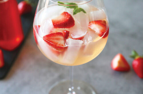 Strawberry Spritz in wine glass with strawberry simple syrup and fresh strawberries and basil